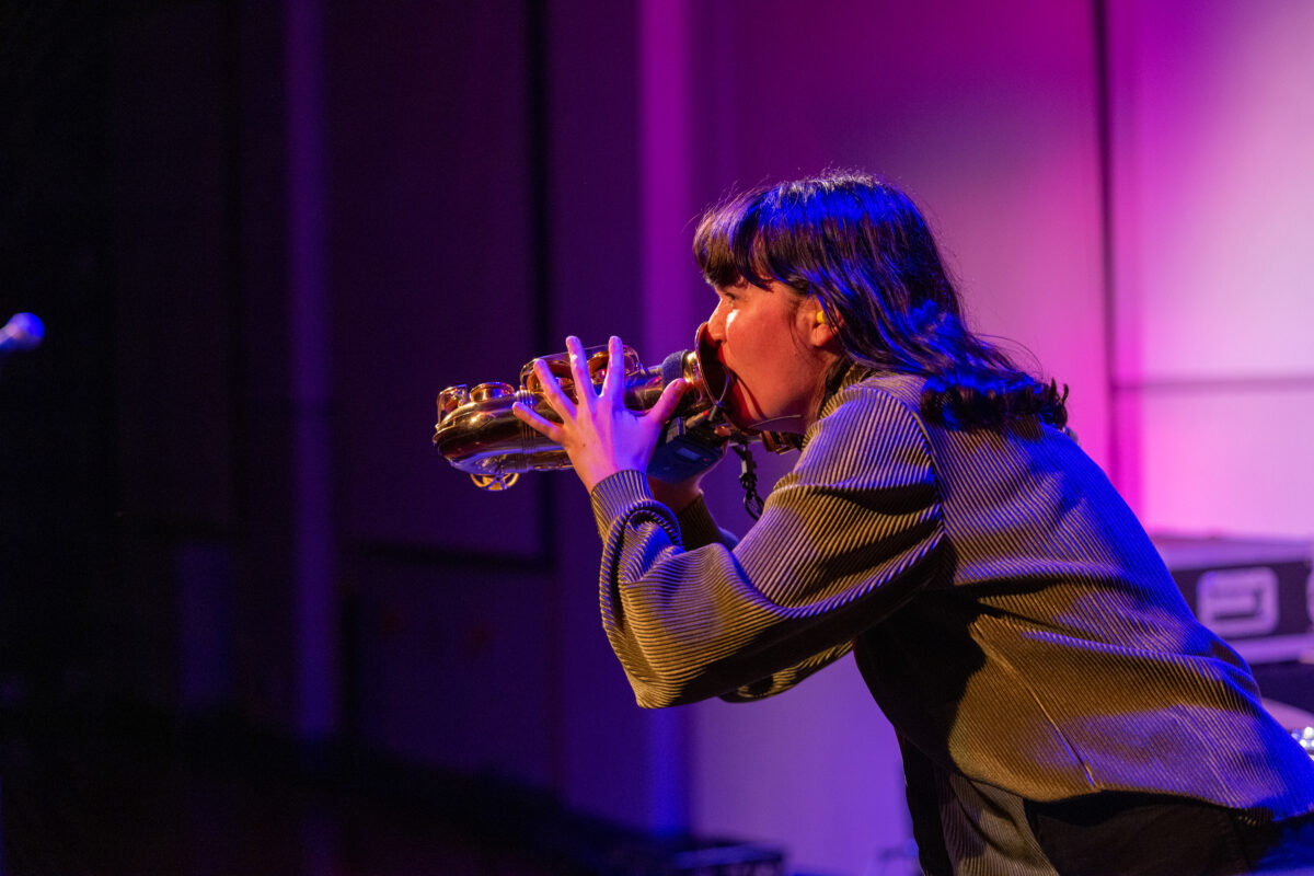 A woman blowing into the mouth of a saxphone