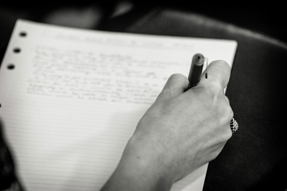 Black and white photo of a hand writing on paper.