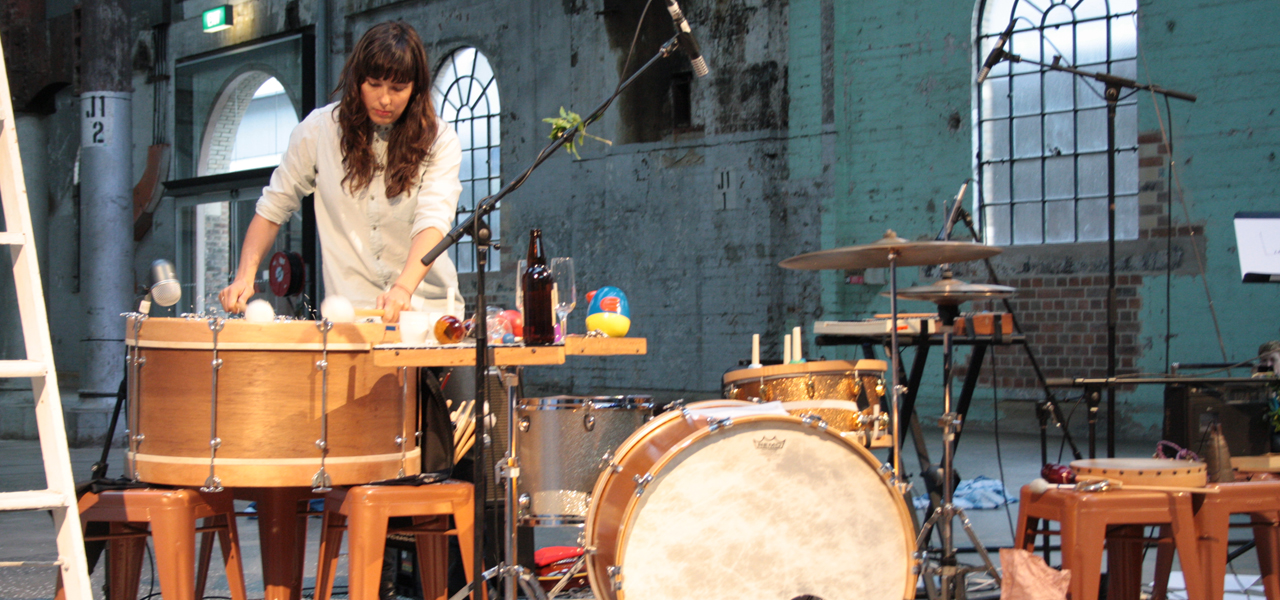 A dark haired female identified standing over a drum kit