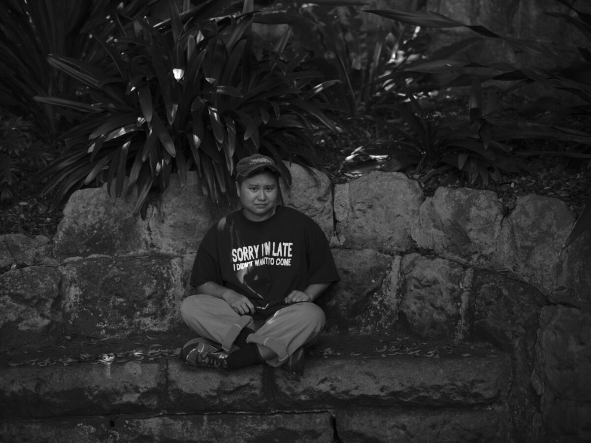 Del Lumanta sits on the ground with a stone wall behind.