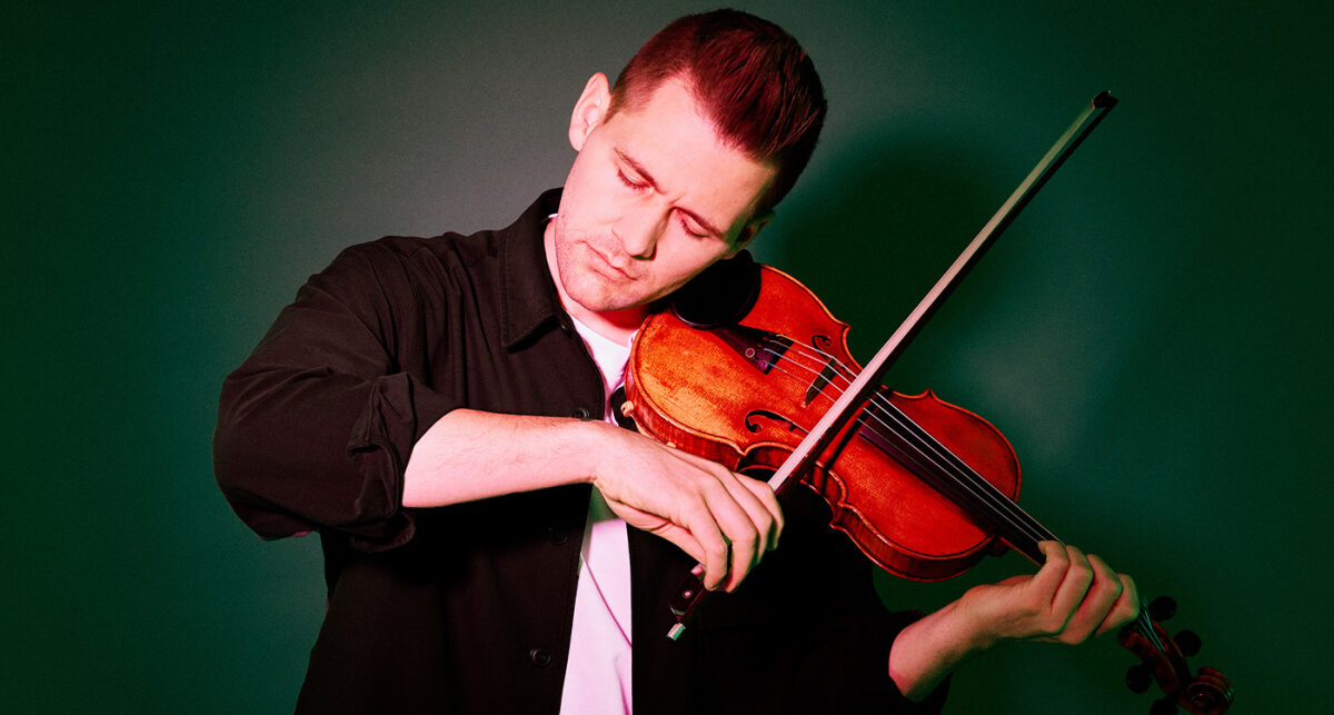 A violinist gently plays with his eyes closed, lit by a soft glowing red light