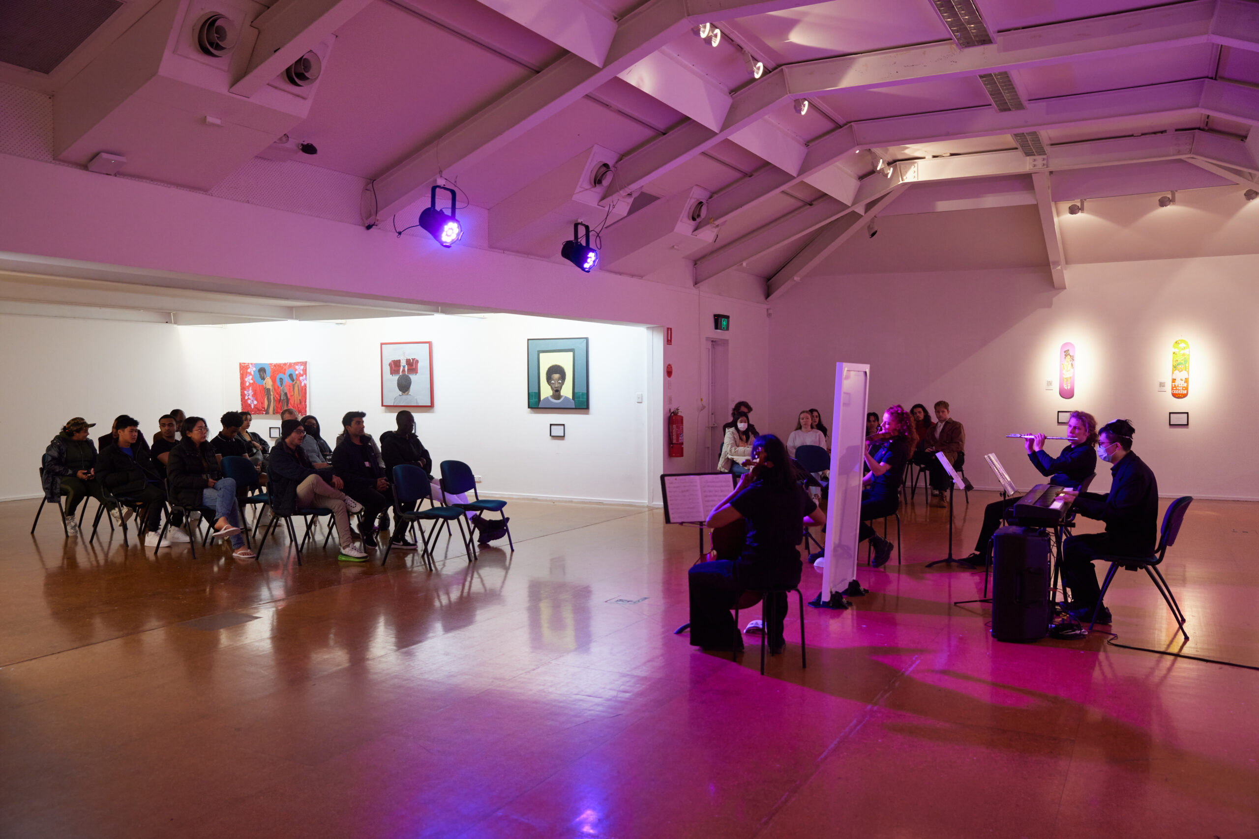 Musicians playing to a crowd in a cool-lit art gallery in Braddon.