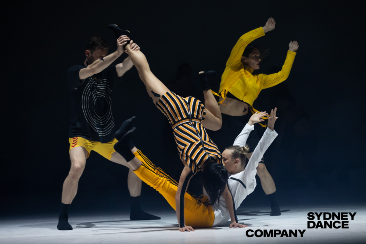 Four Dancers tumble across the stage wearing bright yellow, black and yellow stripes and white shirts