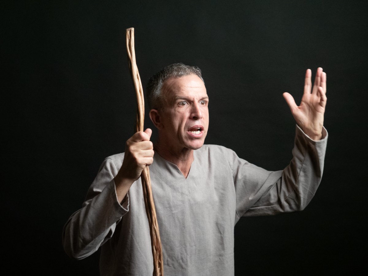 Man stands with arms raised holding a shepherds crook.