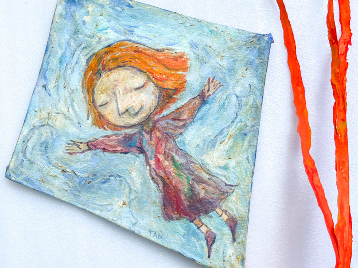 An orange hair girl flies through the air eyes closed. She is an illustration on a small blue kite with a red tail ribbon.