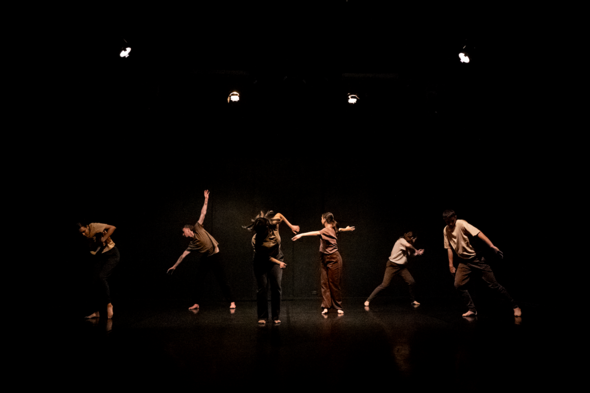 Dancers strike a pose on a dimly lit stage in almost darkness.