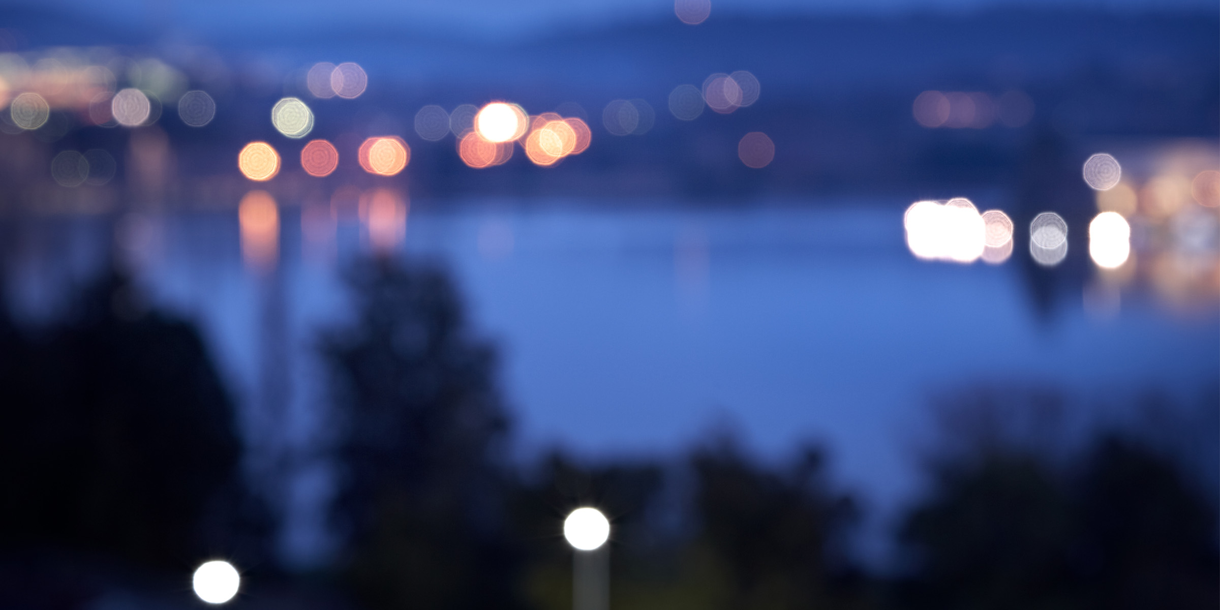 Blurred image of a lake at dusk surrounded by city lights.