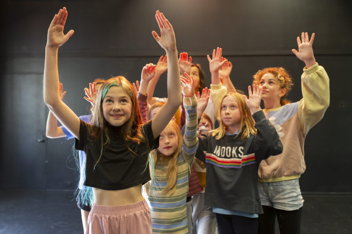 A group of young actors play in a theatre space.