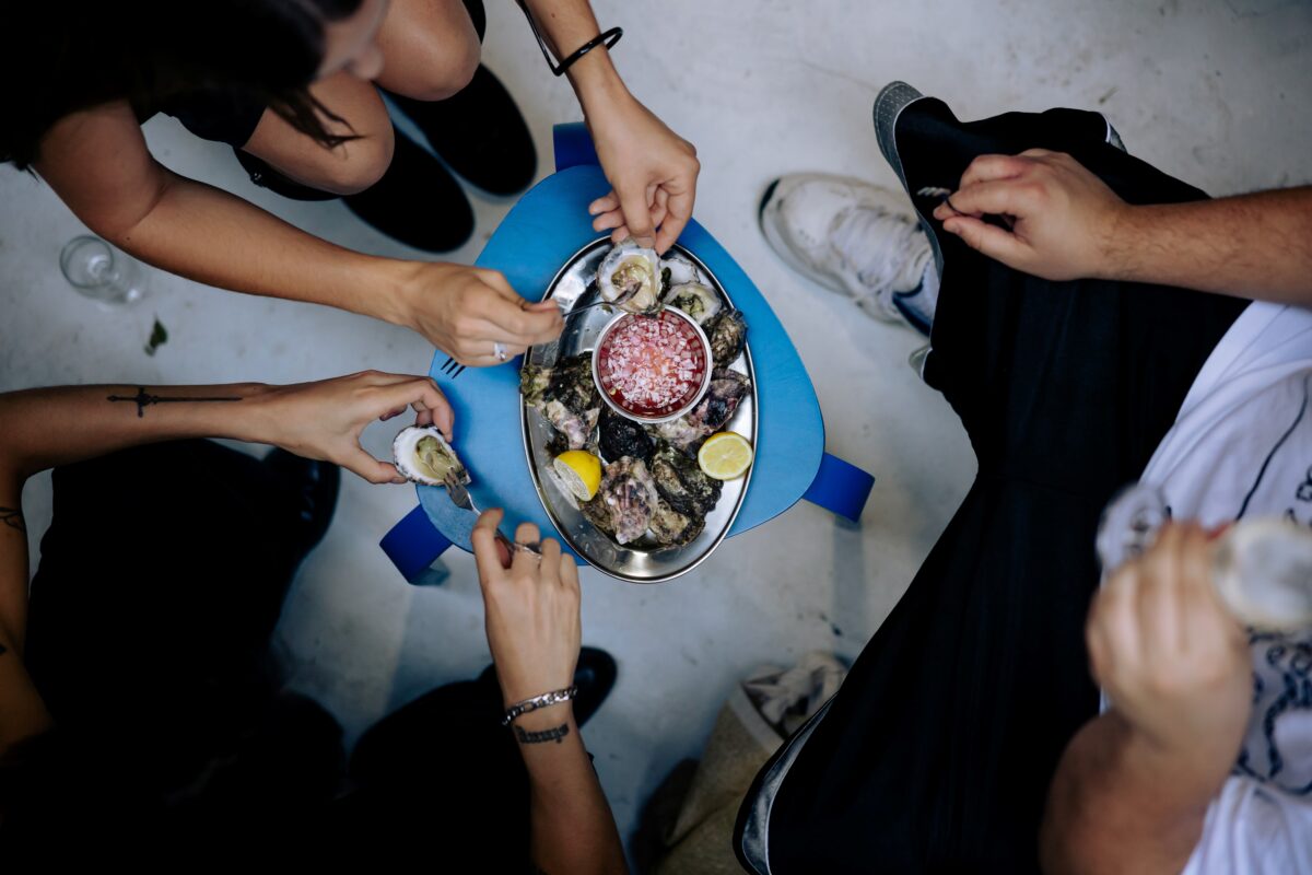 A plate of oysters sits in the middle of a group of people, shot from above.