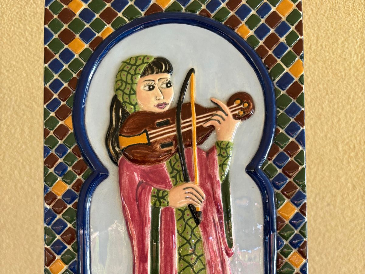 A delicate painted ceramic artwork of a violin play surrounded by moorish style arch.