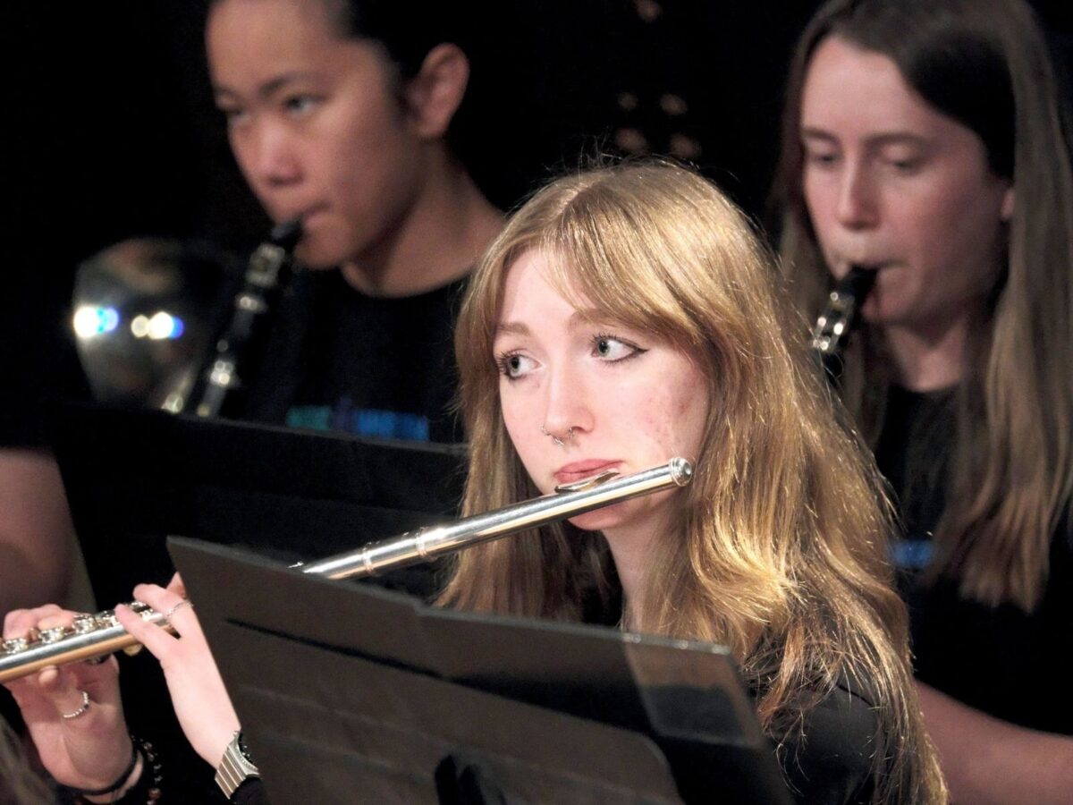 A close-up image of a flutist playing on stage wearing black.