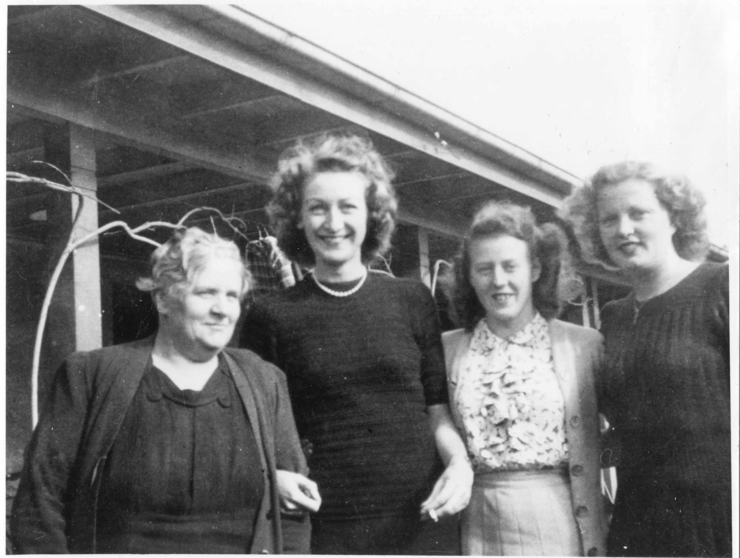 Four ladies stand arm in arm smiling at the camera, circa 1940-1955.