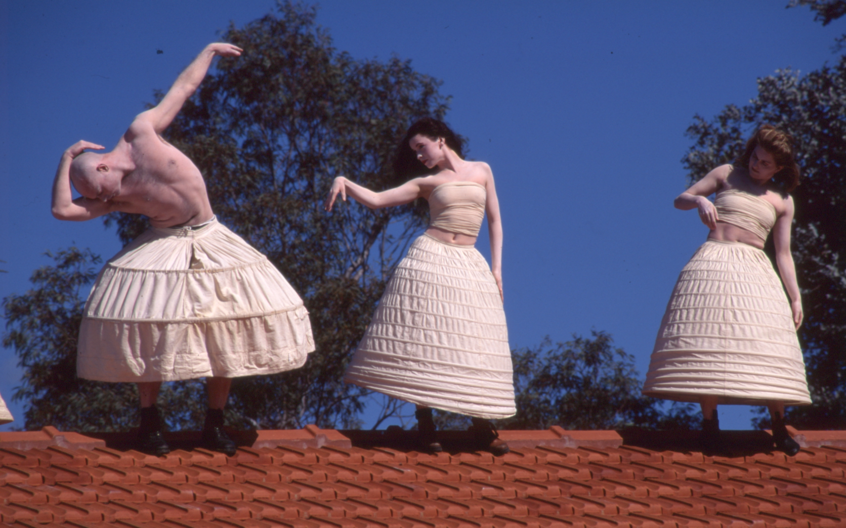 Three dancing figures in wide white hoop skirts dance on the red brick roofs of Gorman House.